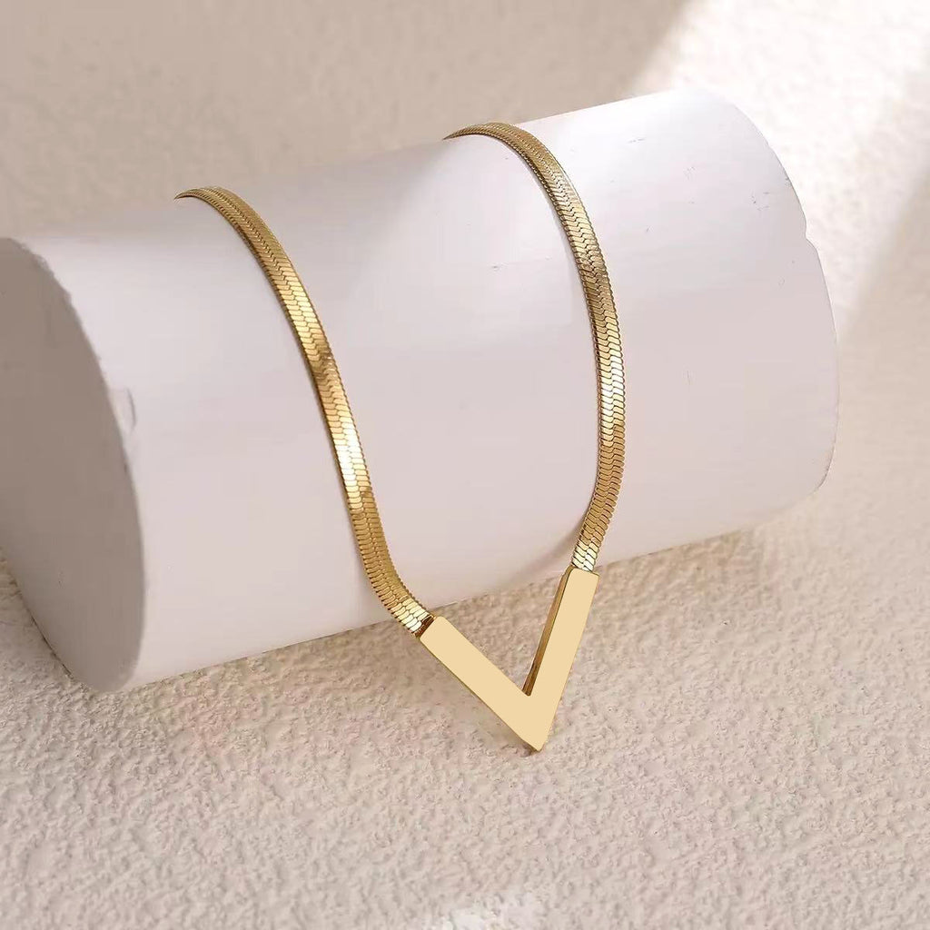 Gold V-shaped herringbone snake chain necklace draped over white cylinder display stand on beige background