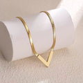 Gold V-shaped herringbone snake chain necklace draped over white cylinder display stand on beige background