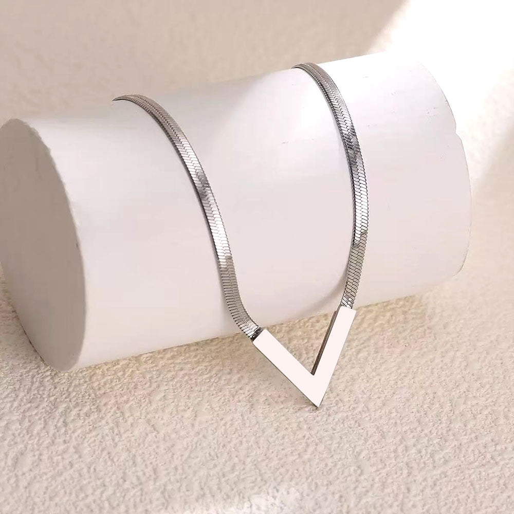 Silver V-shaped herringbone snake chain necklace draped over white cylinder display stand on beige background