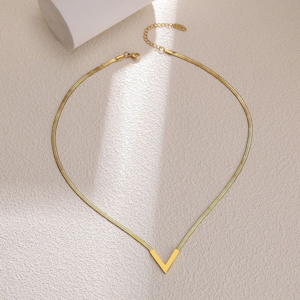 Gold V-shaped snake chain necklace laid flat on beige surface showing lobster clasp and extender chain detail