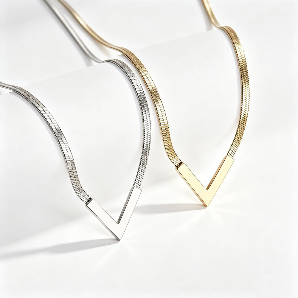 Close-up of gold and silver V-shaped snake chain necklaces showing polished herringbone texture and V pendant detail