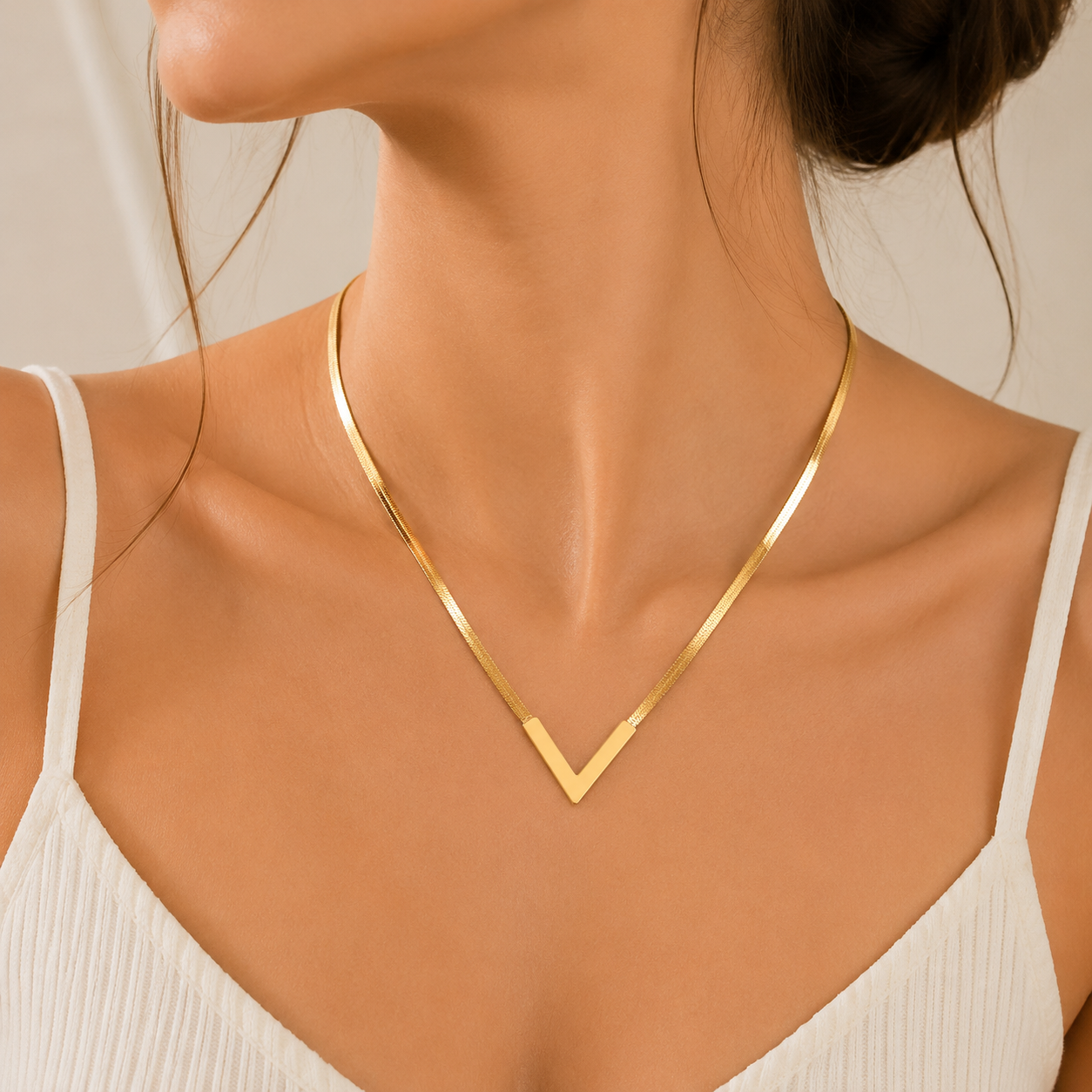 Woman wearing gold V-shaped snake chain necklace on collarbone with white top — elegant everyday jewelry look